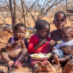 two african children in a village near Kalahari desert, the sister feeding her brother in the outdoors kitchen